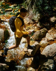 Person hiking through a rocky stream wearing a yellow shirt and black backpack.