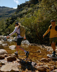 Two hikers crossing a stream in a mountainous area