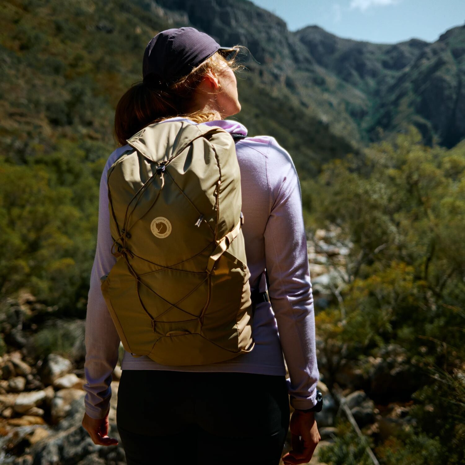Person with a beige backpack looking at a mountainous landscape