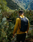 Person in a yellow jacket with a black backpack walking through a forested area.