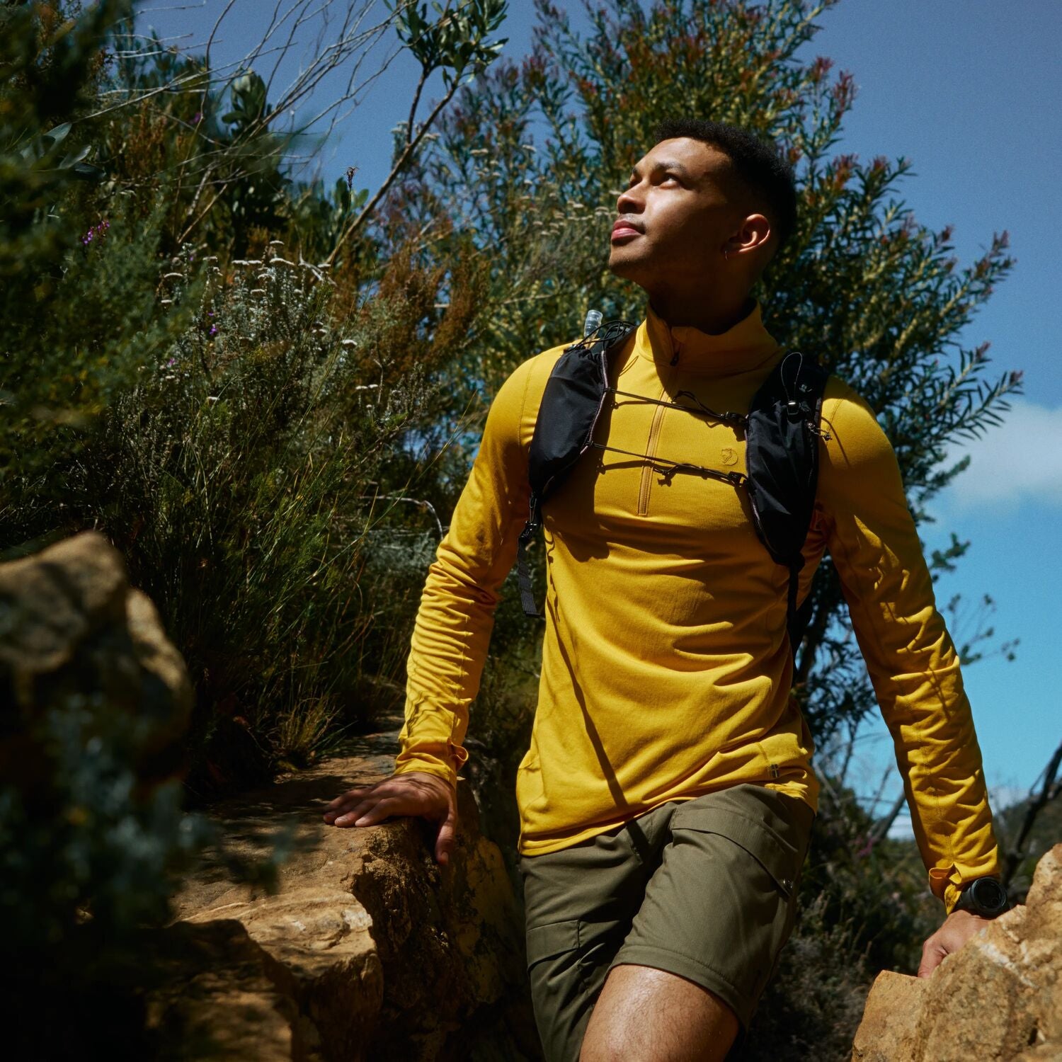 Man hiking on a trail with greenery and clear sky