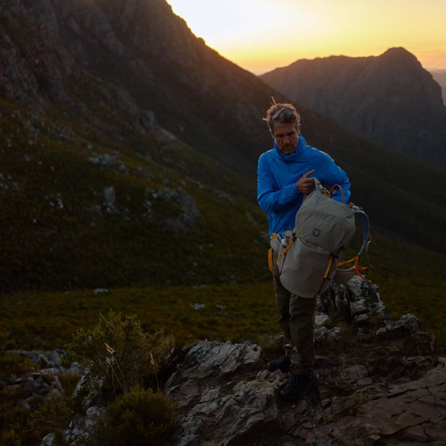 Person standing on a mountain peak with a backpack at sunset
