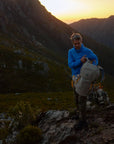 Person standing on a mountain peak with a backpack at sunset