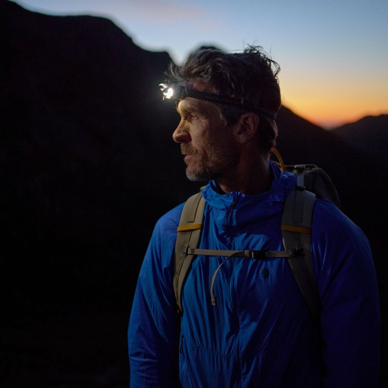 Man in blue jacket with headlamp on mountain at sunset