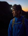 Man in blue jacket with headlamp on mountain at sunset
