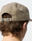 Beige cap with a small flag emblem on the back, worn by a person with short brown hair.