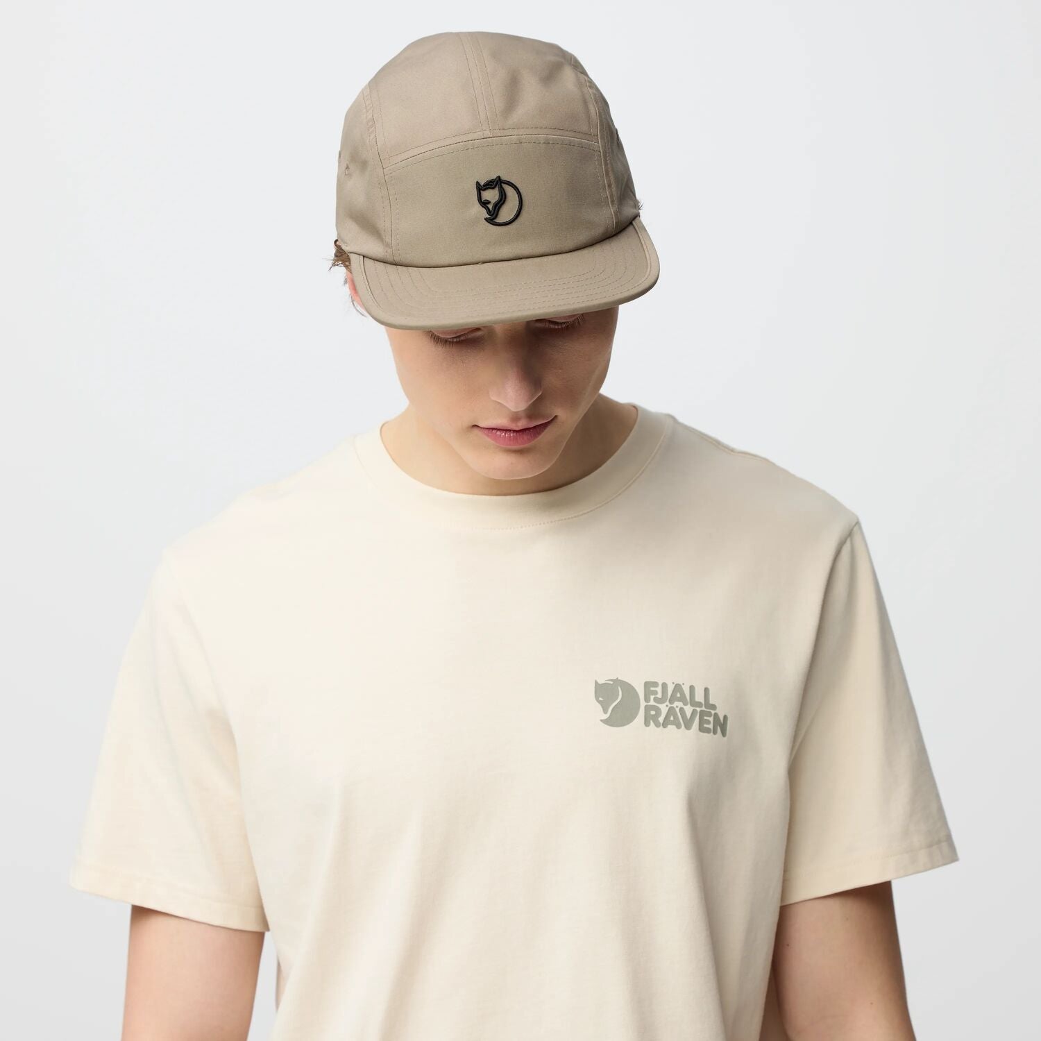 Person wearing a beige cap and t-shirt with a arctic fox logo on a light gray background