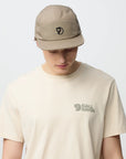 Person wearing a beige cap and t-shirt with a arctic fox logo on a light gray background