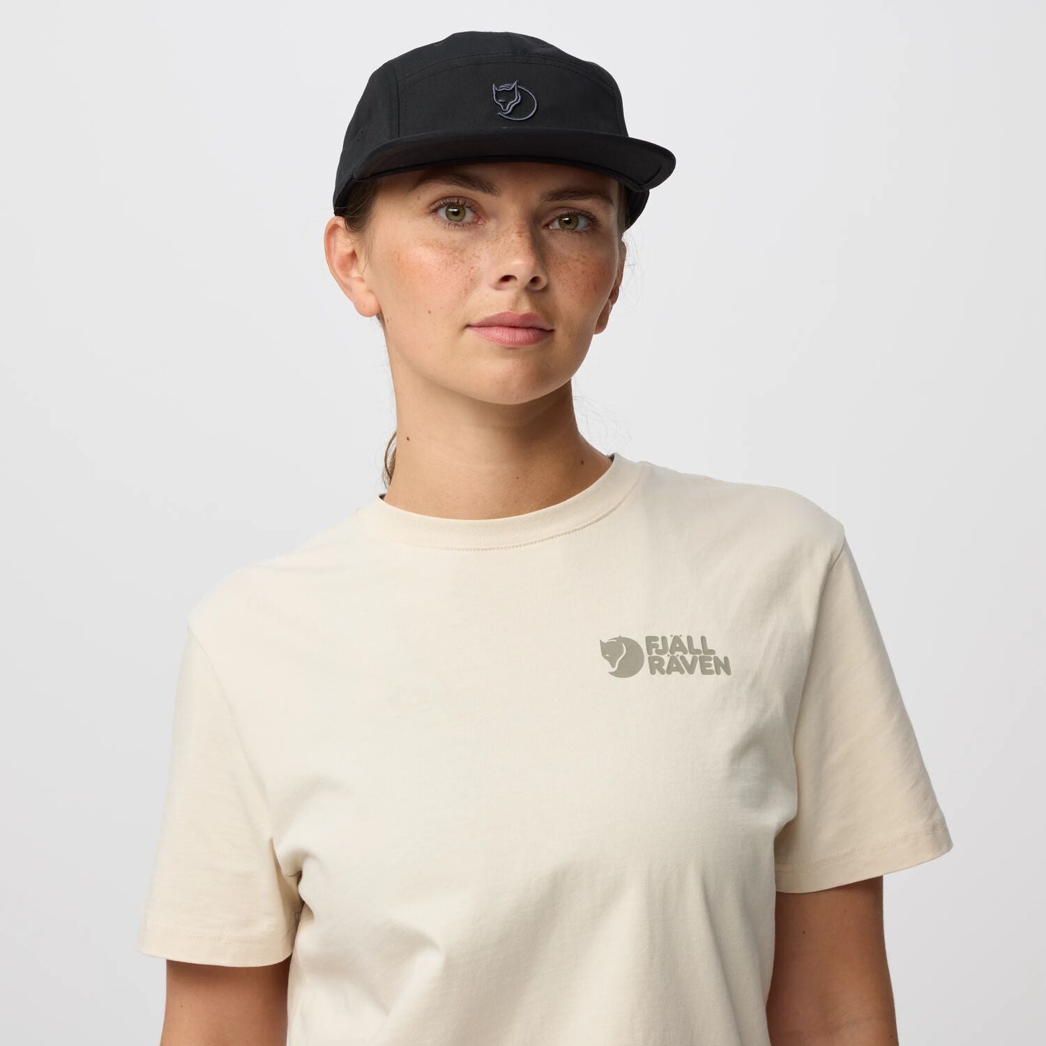 Person wearing a black cap and beige t-shirt with a arctic fox logo on a light gray background