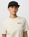 Person wearing a black cap and beige t-shirt with a arctic fox logo on a light gray background