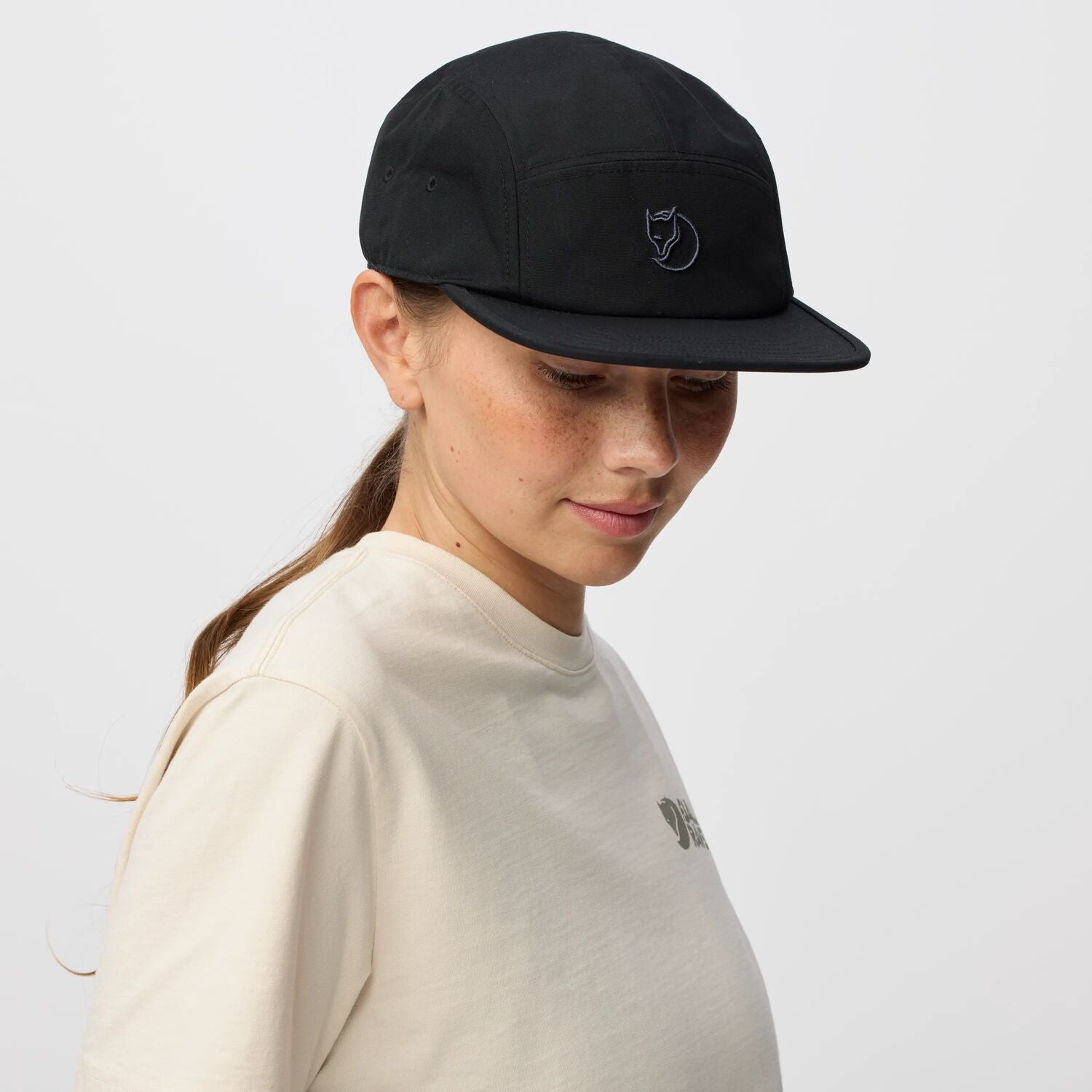 Person wearing a black cap with a arctic fox logo on a light gray background