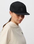 Person wearing a black cap with a arctic fox logo on a light gray background