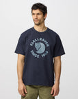 Man wearing a navy t-shirt with a Fjällräven  logo and text on a white background