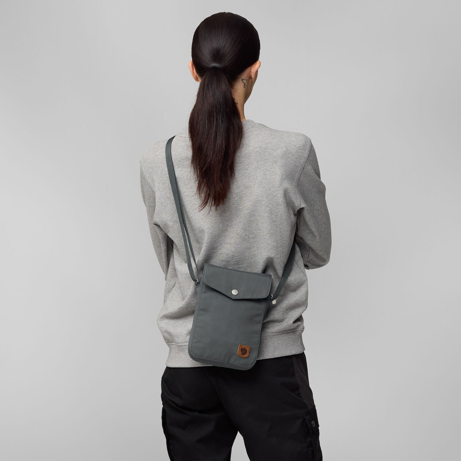 Person wearing a gray crossbody bag on a plain background