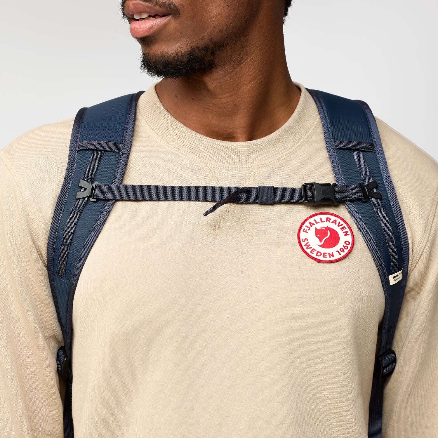 Person wearing a navy backpack with a visible Fjällräven logo on a plain background