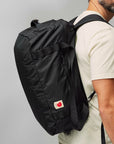 Person wearing a black backpack with a visible Fjällräven logo on a plain background