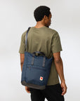 Person wearing a blue backpack totepack on a plain background