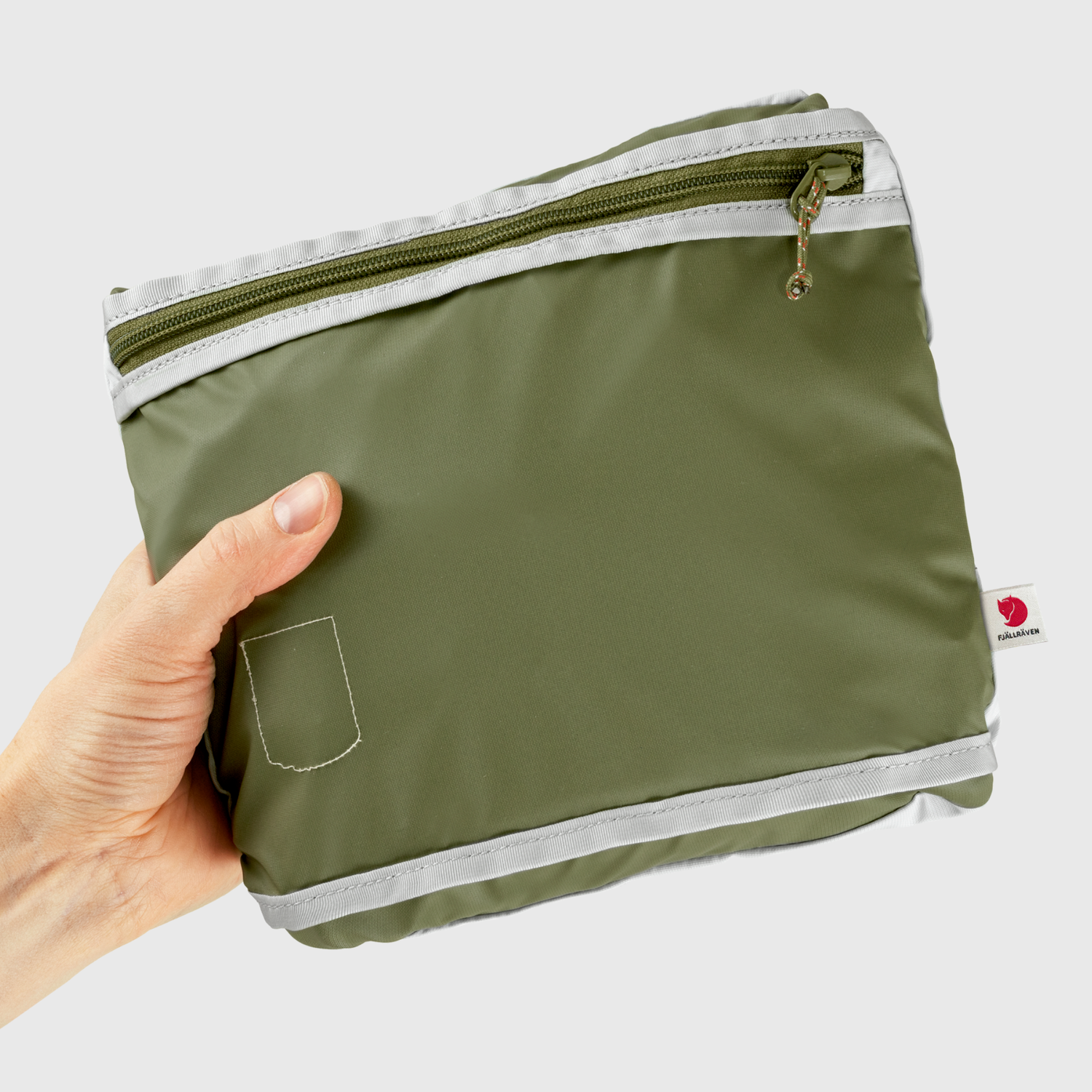 Green travel pouch with a zipper held by a hand on a light gray background