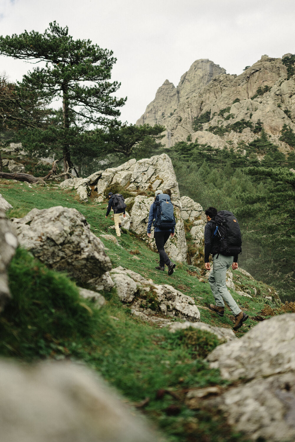 Three hikers with backpacks walking on a rocky mountain trail.