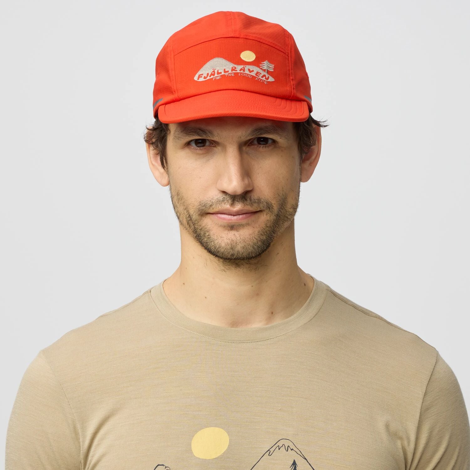 Man wearing a red cap and beige t-shirt with a logo on a light gray background