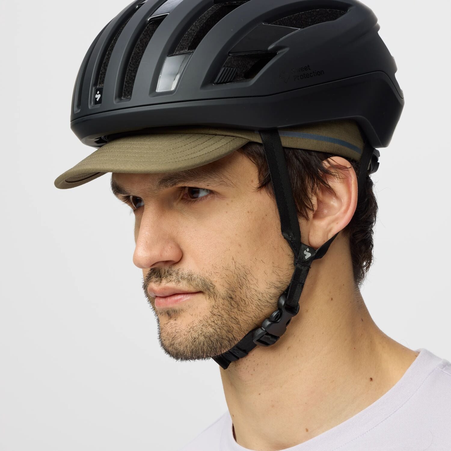 Person wearing a black helmet and beige cap on a light gray background