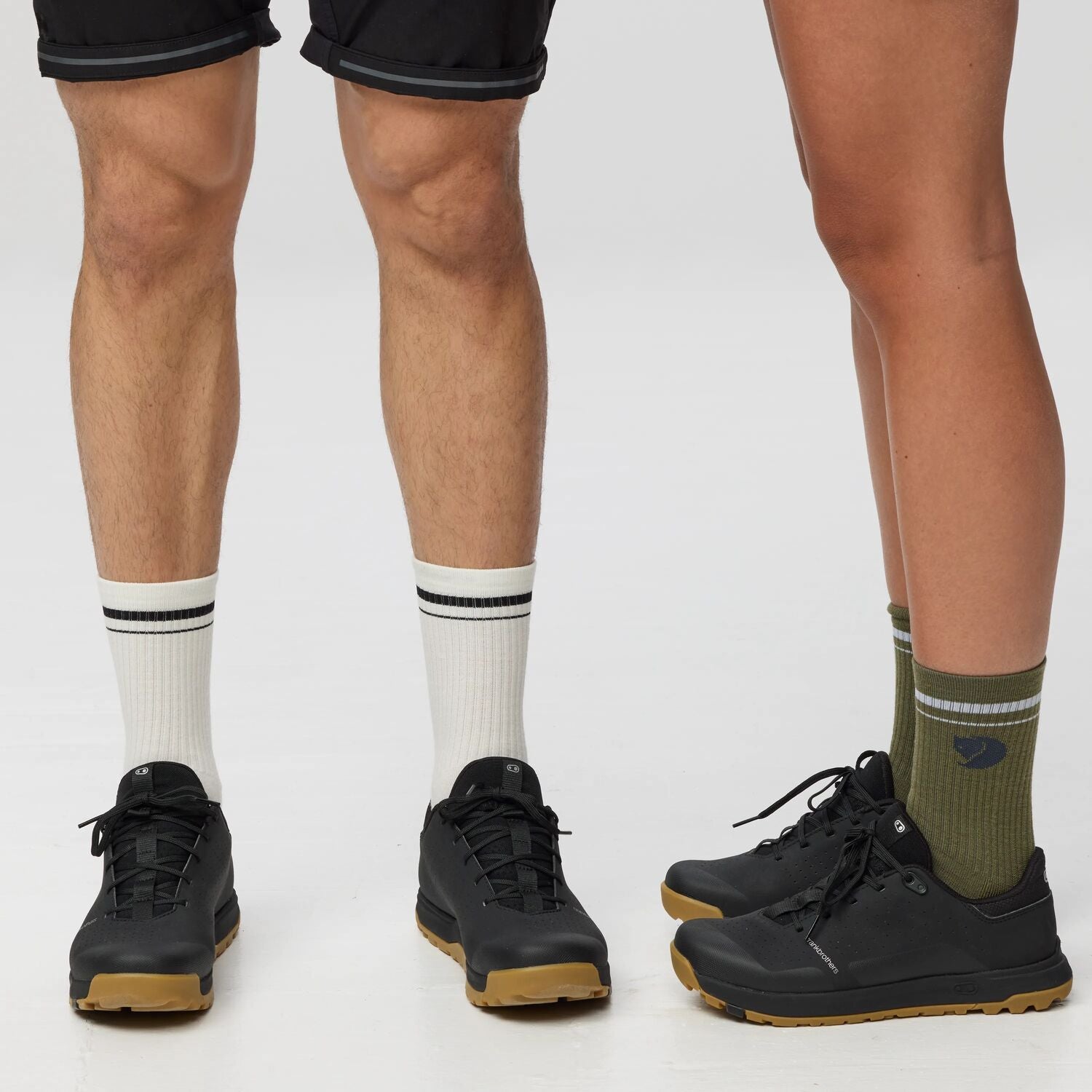 Two pairs of legs wearing different socks and shoes on a plain background