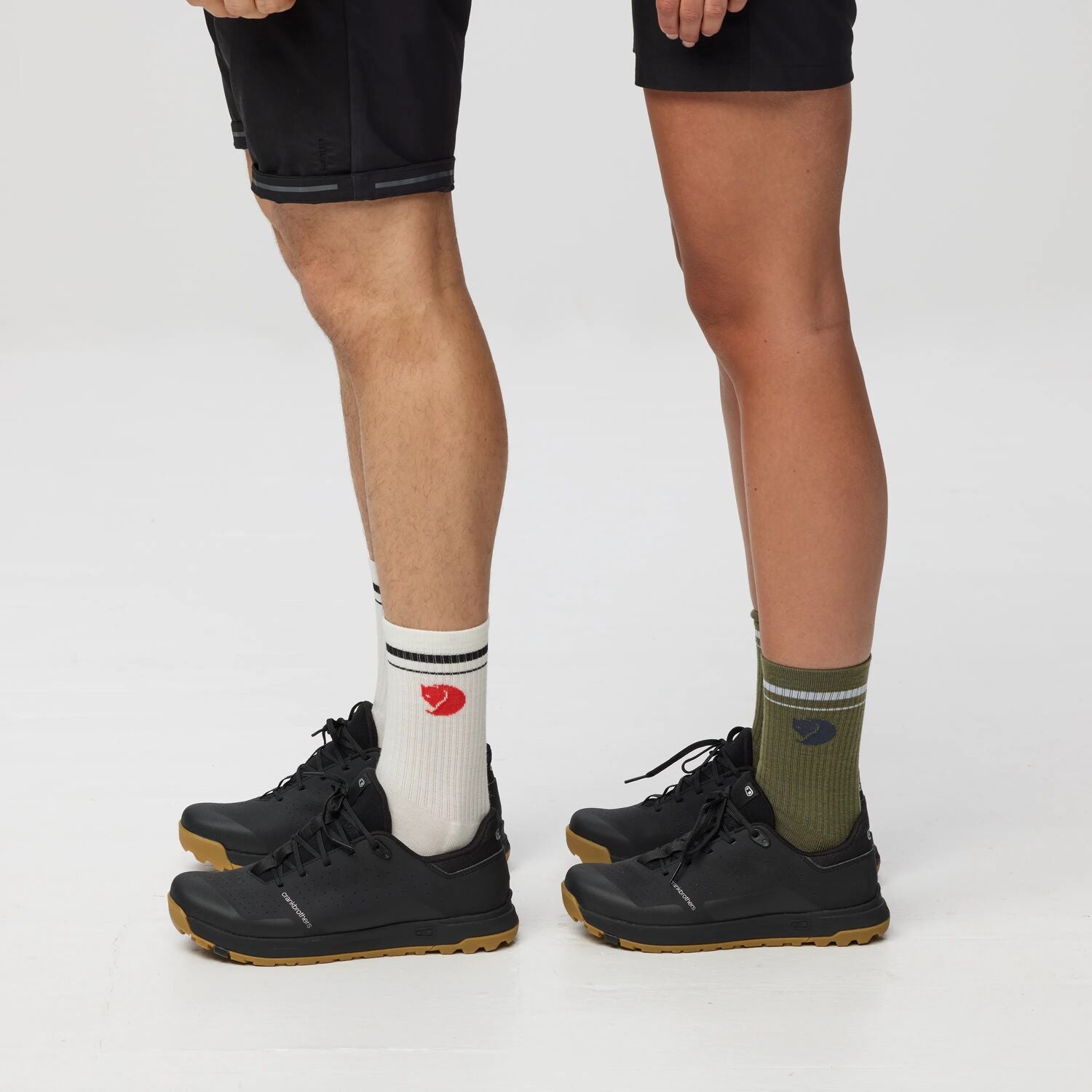 Two pairs of legs wearing black shoes and colorful socks on a white background