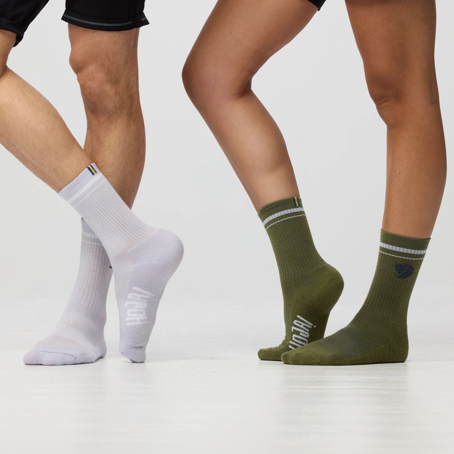 Two pairs of legs wearing white and green socks on a light gray background