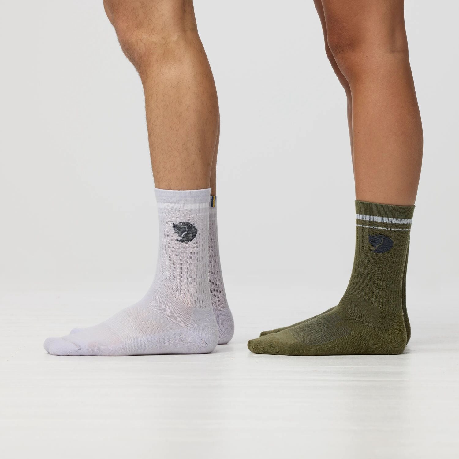 White and green socks with a fjallraven logo worn by a person on a light gray background