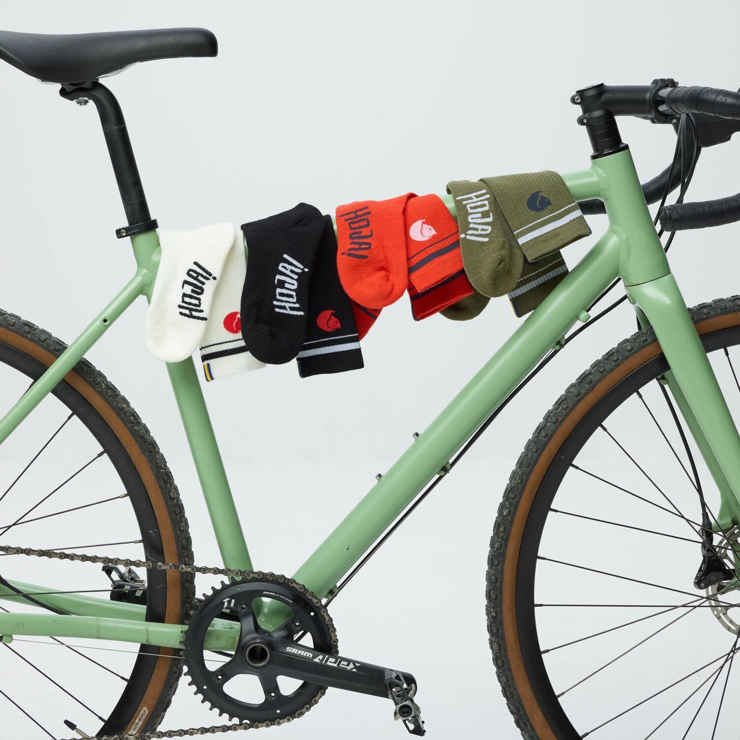 Set of colorful socks hanging on a green bicycle against a light gray background