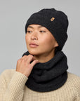 Person wearing a black knit beanie and scarf against a gray background