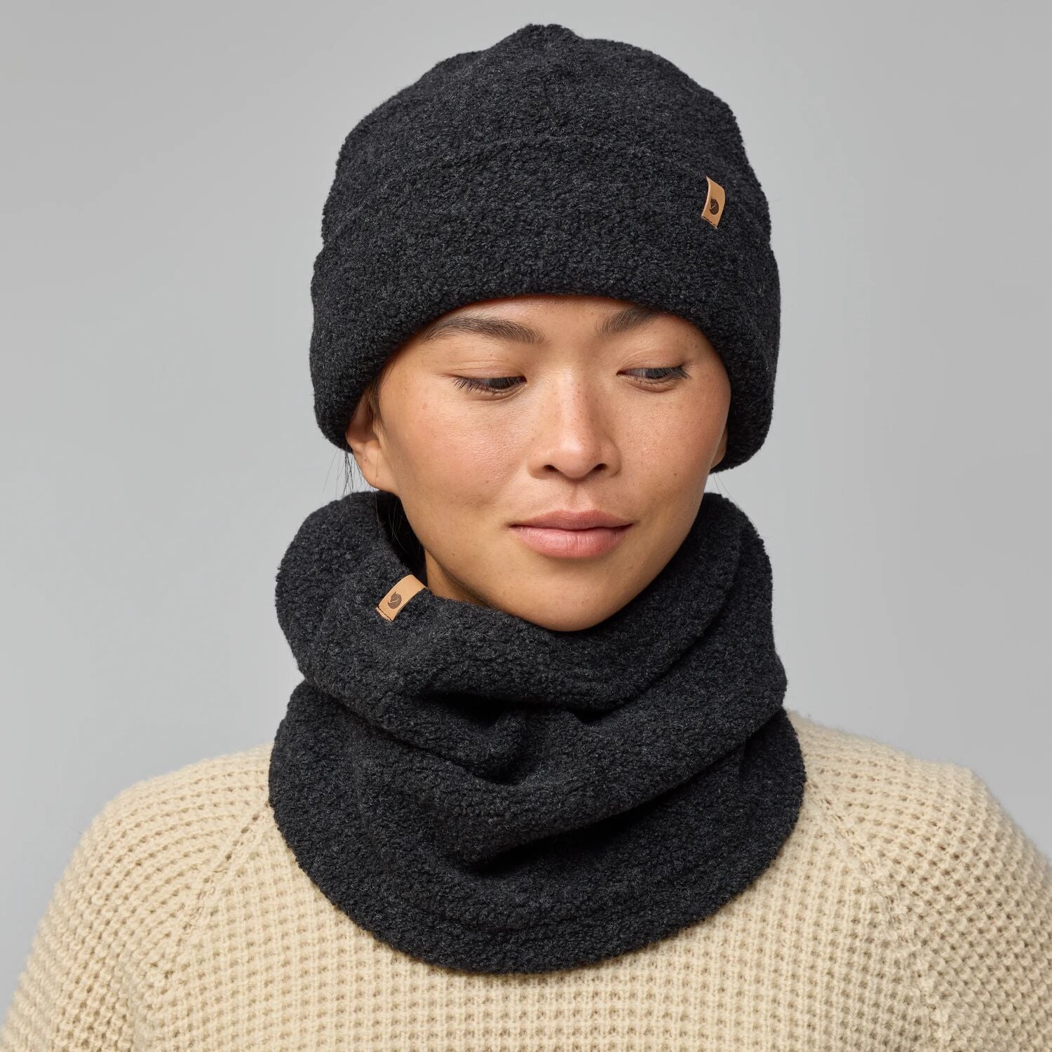 Person wearing a dark gray knit beanie and scarf on a gray background