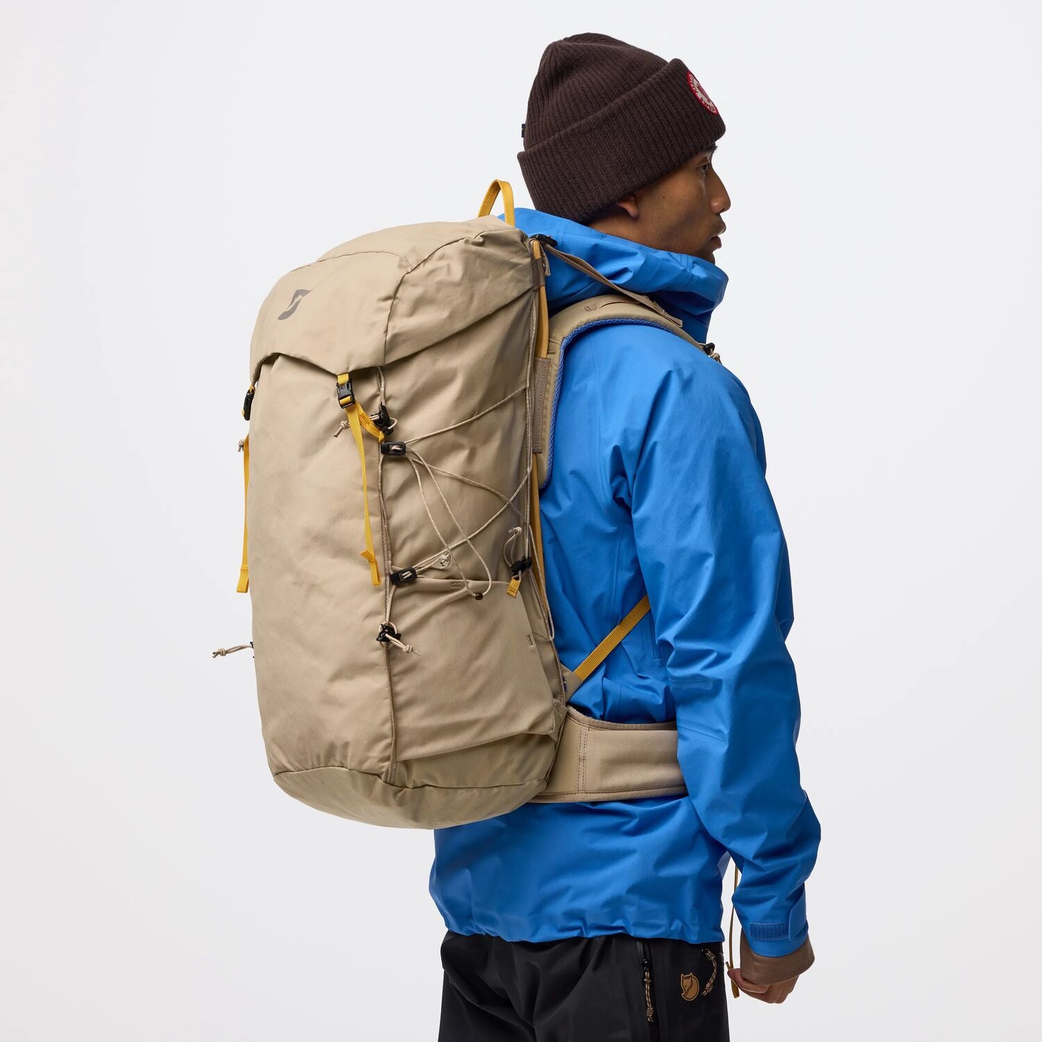 Person wearing a blue jacket and brown beanie with a beige backpack on a white background
