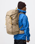Person wearing a blue jacket and brown beanie with a beige backpack on a white background