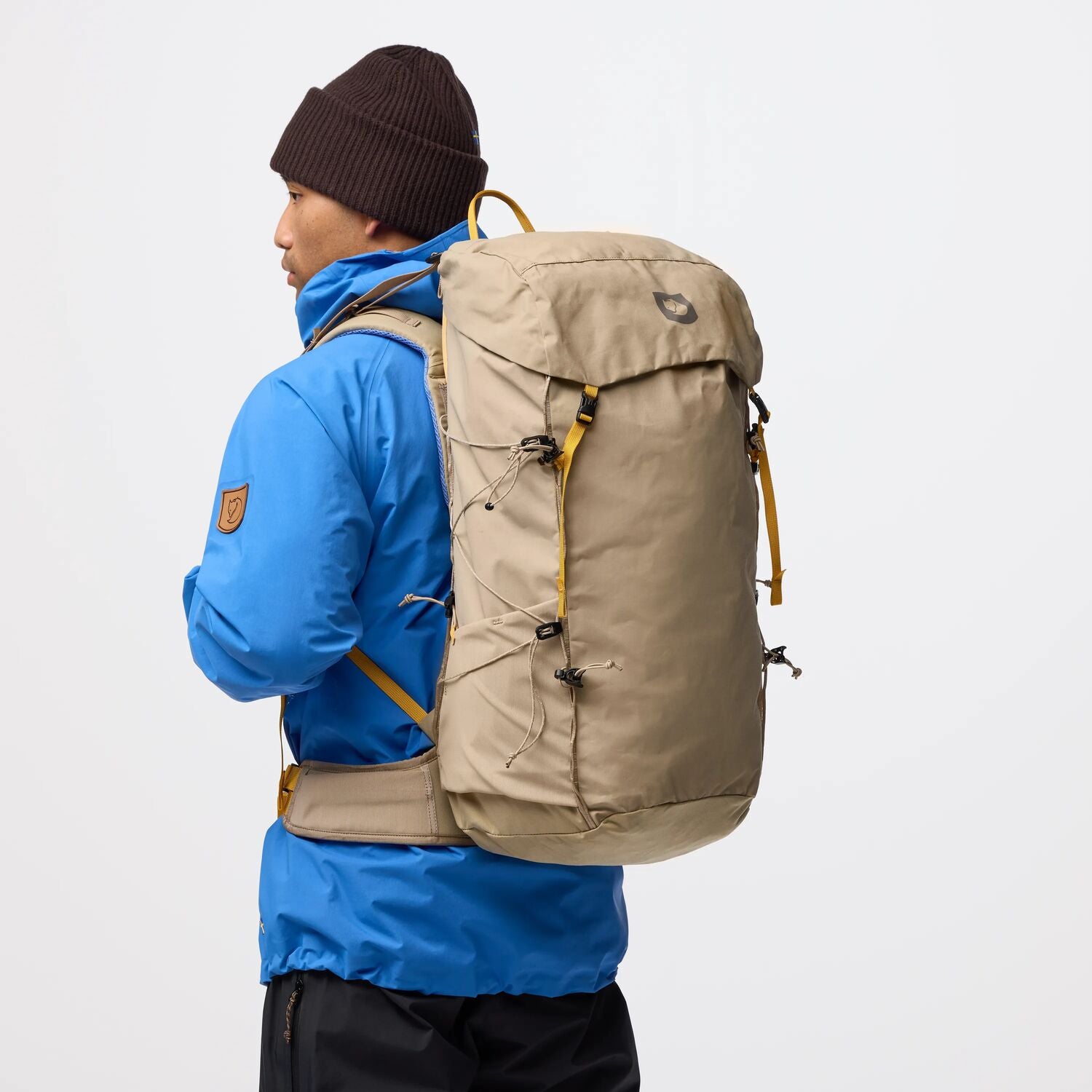 Person wearing a blue jacket and brown backpack on a white background