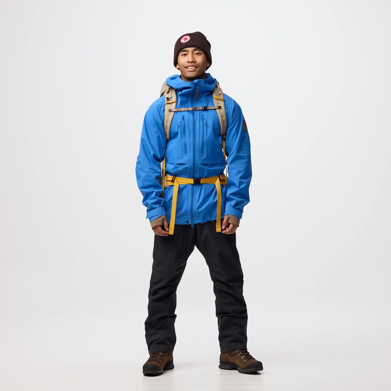 Person wearing a blue jacket, black pants, and a brown backpack on a white background