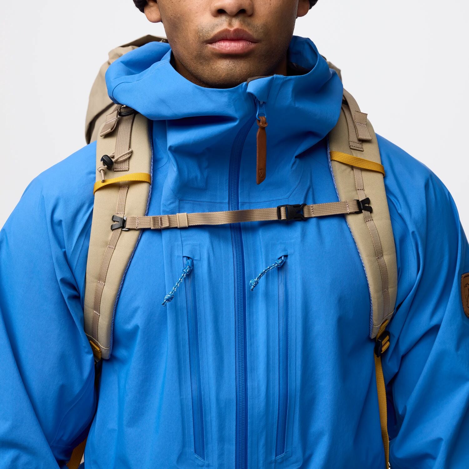 Person wearing a blue jacket with a beige backpack on a light gray background