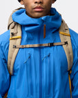 Person wearing a blue jacket with a beige backpack on a light gray background