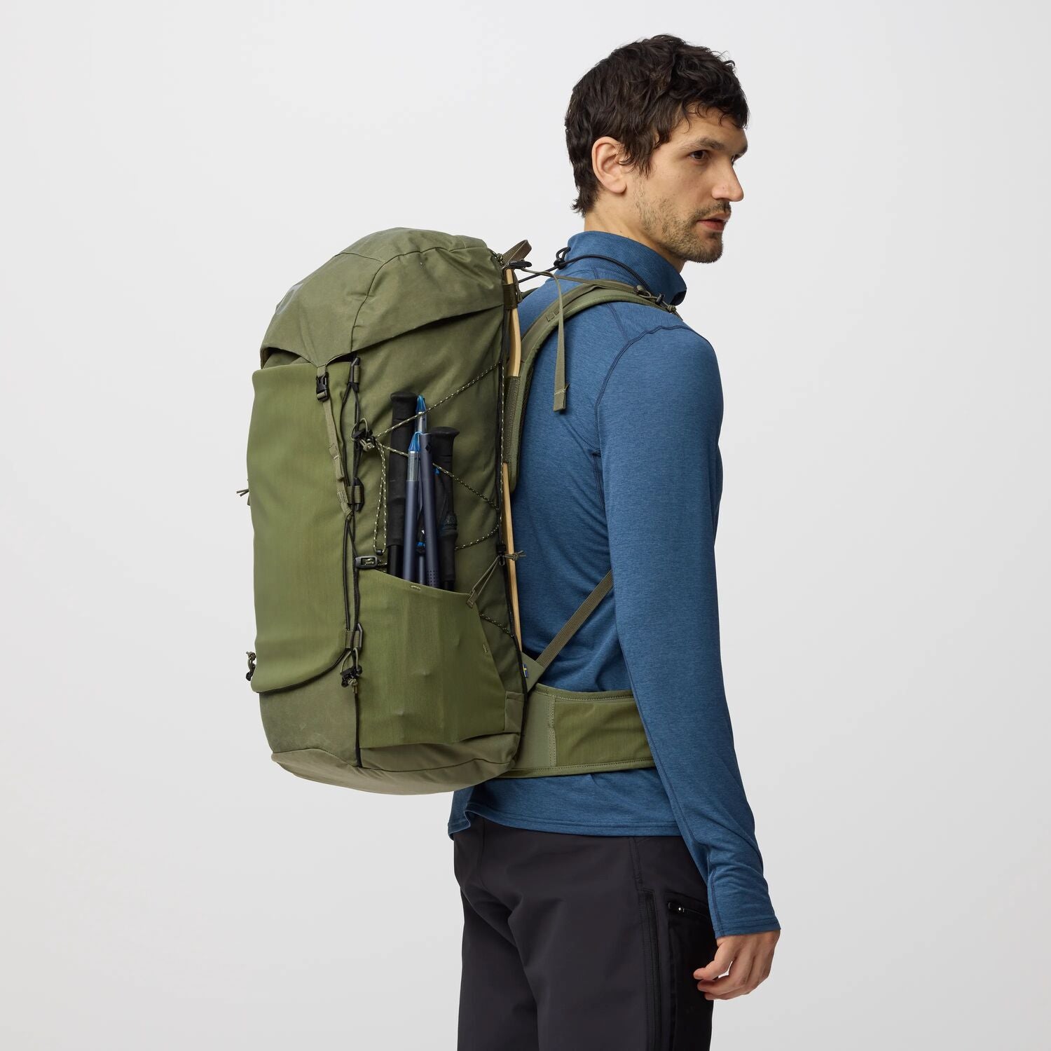 Man wearing a green backpack on a light gray background with hiking accessories