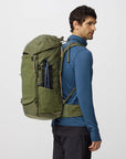 Man wearing a green backpack on a light gray background with hiking accessories