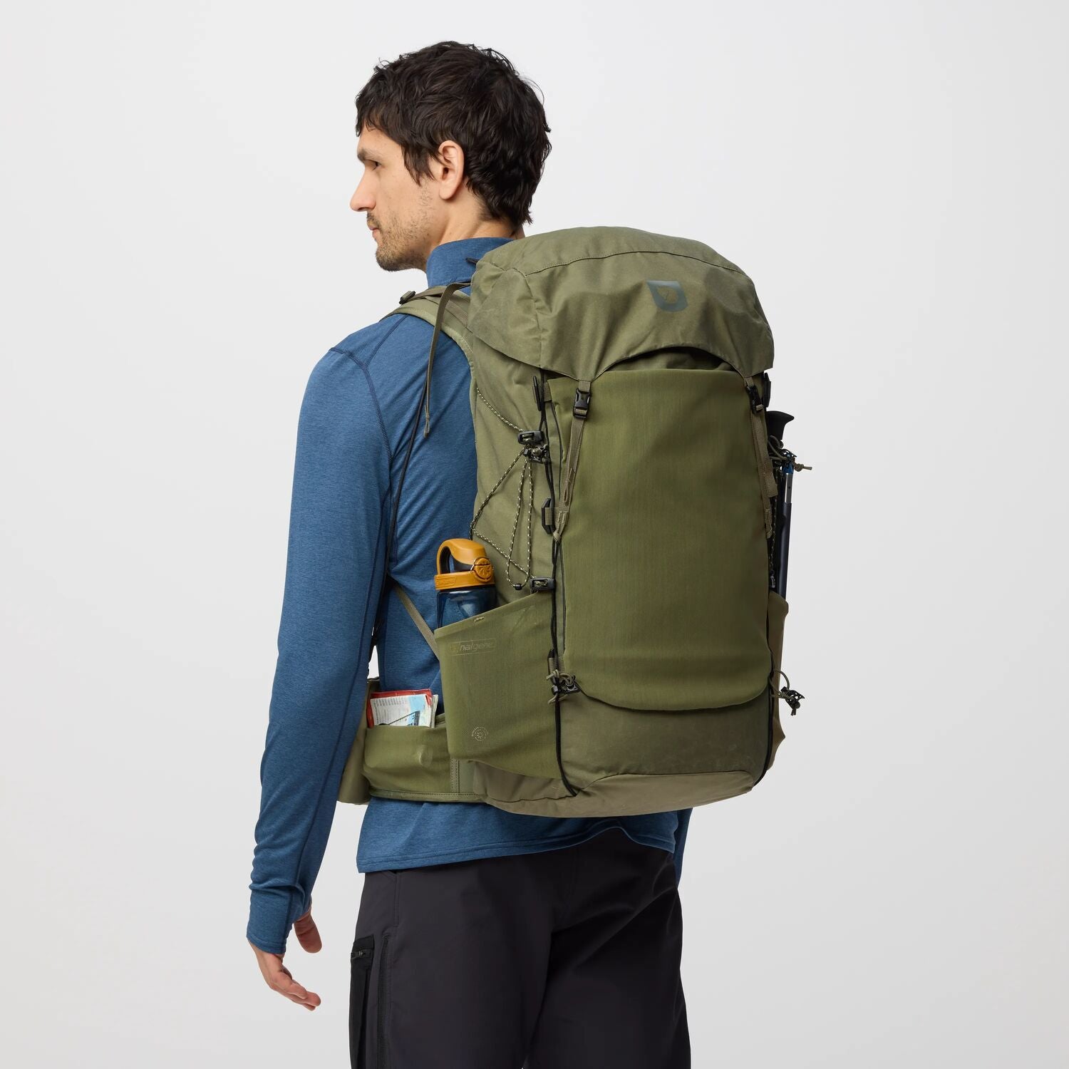 Man wearing a green backpack on a plain background