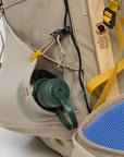 Close-up of a beige backpack with a green water bottle and wooden stability structure, on a white background.
