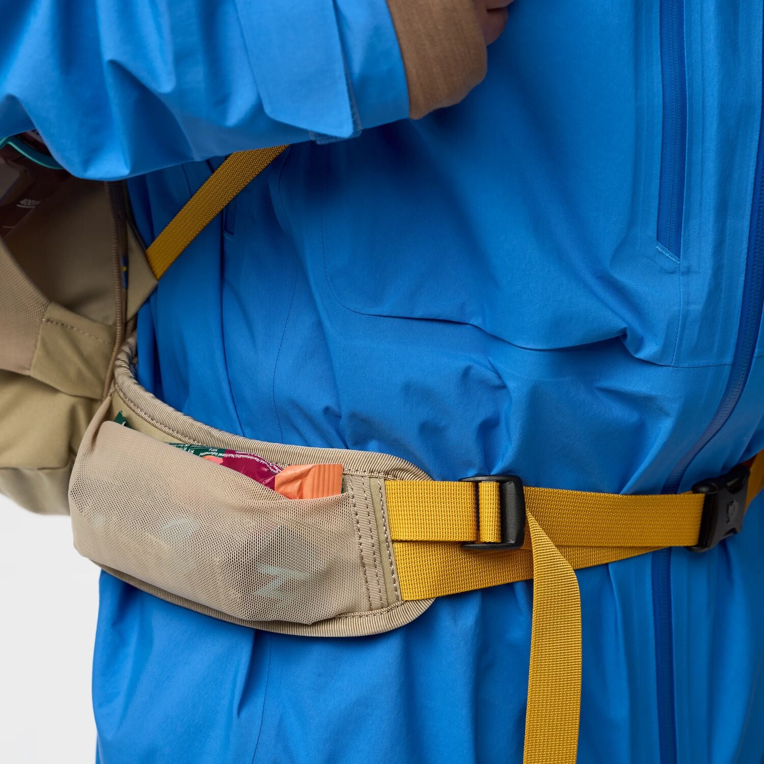 Person wearing a blue jacket with a beige pocket bag and yellow strap on a white background
