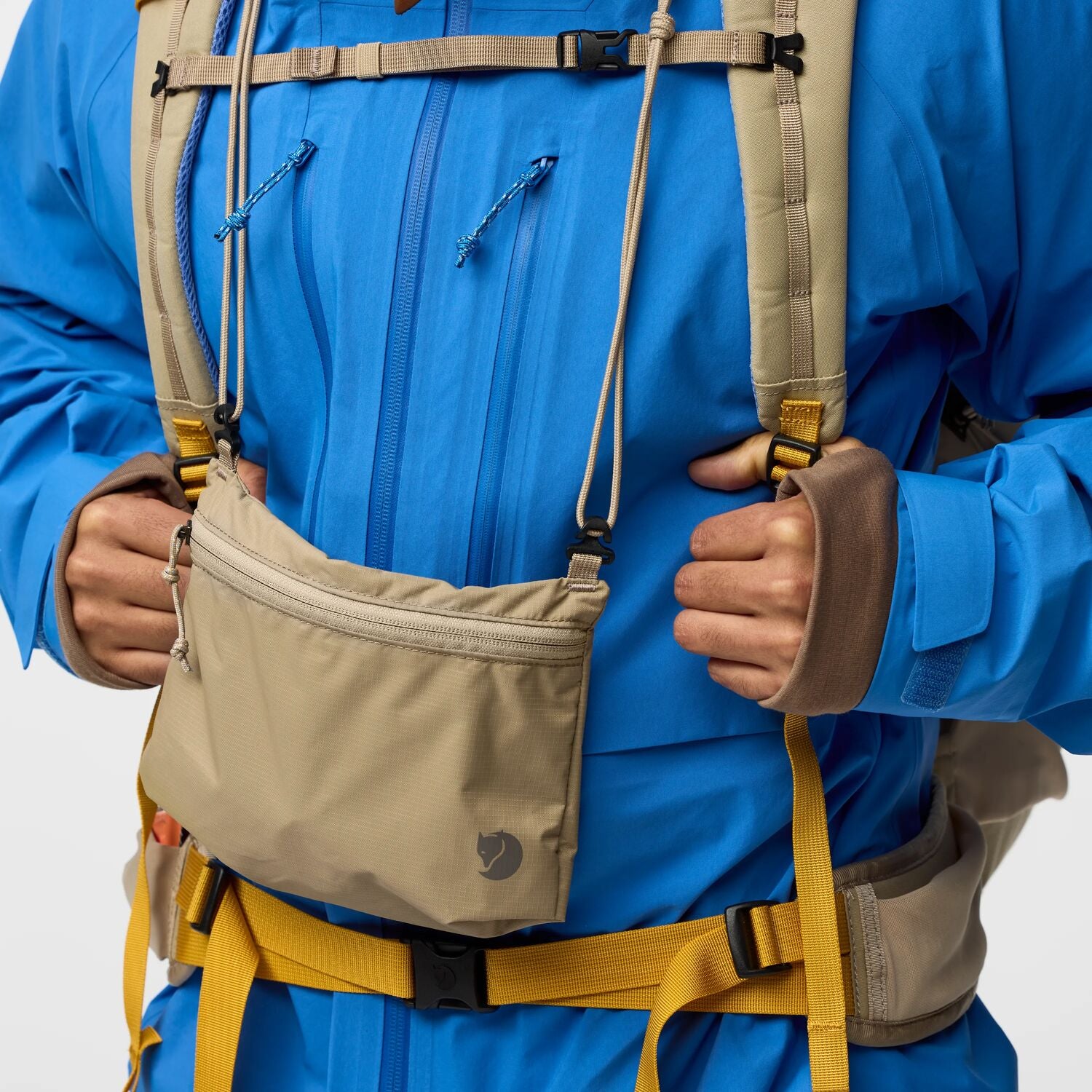 Person wearing a blue jacket with a beige sling pouch on a white background