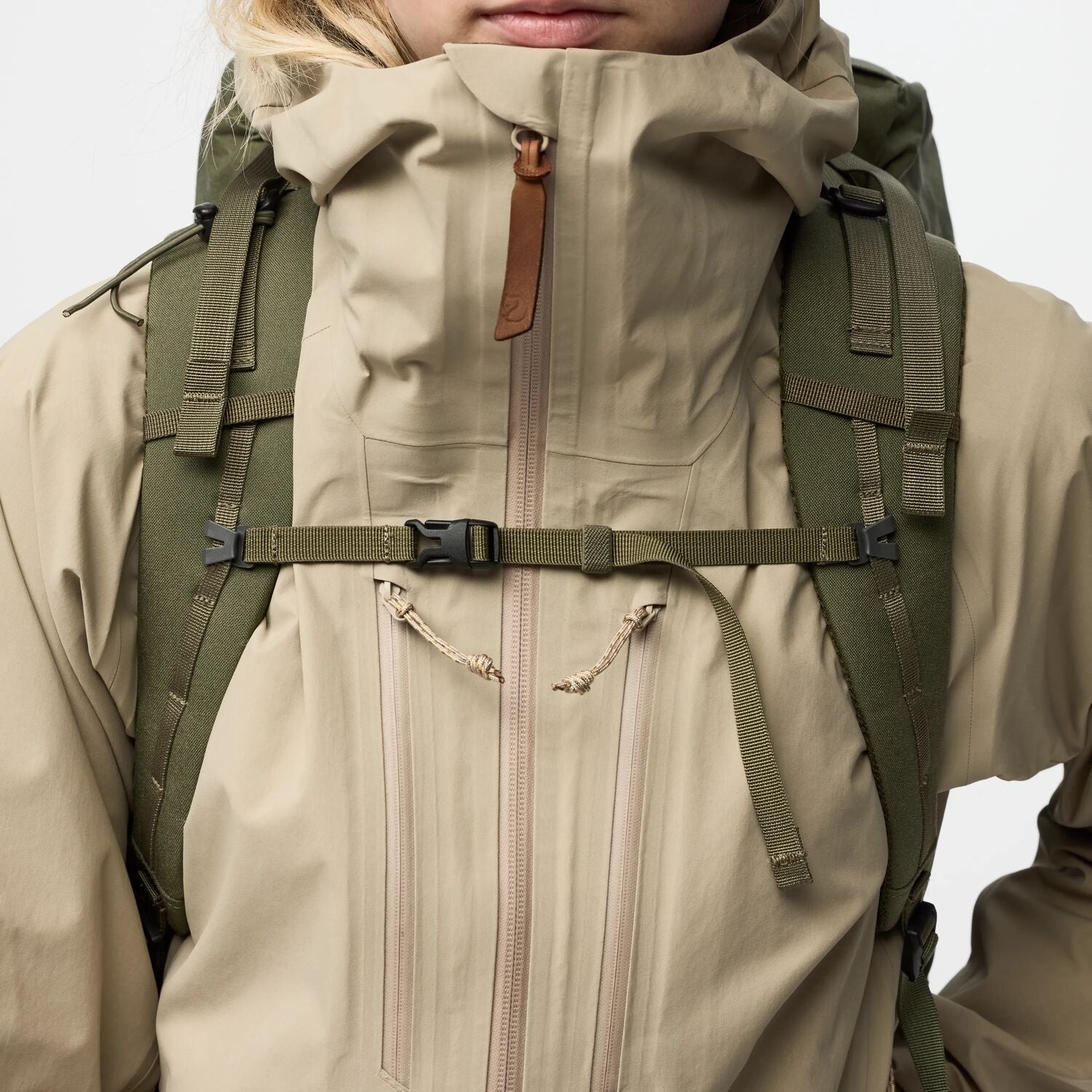 Person wearing a beige jacket and green backpack on a white background