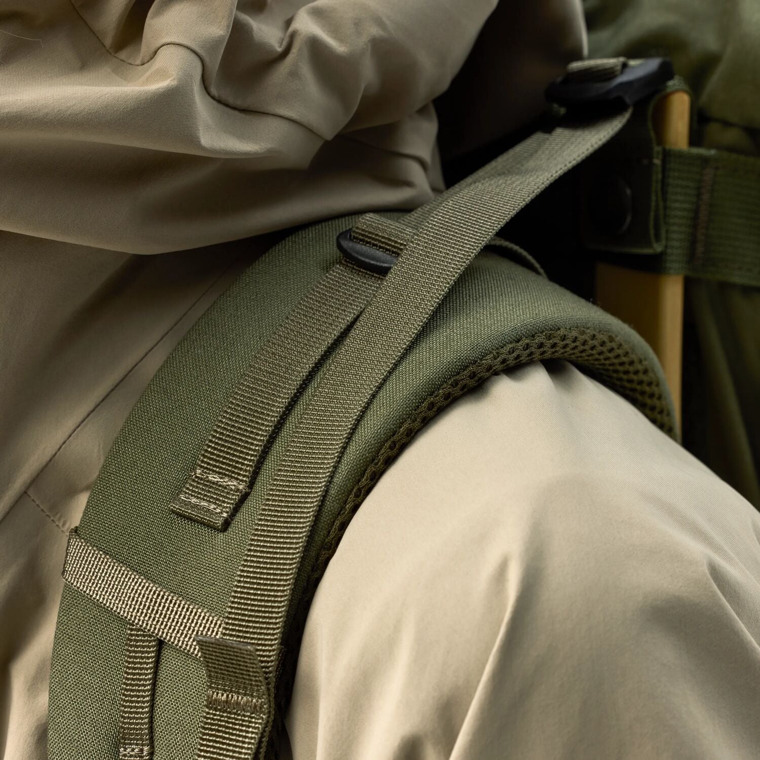 Close-up of a green backpack strap on a person wearing a beige jacket.
