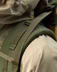 Close-up of a green backpack strap on a person wearing a beige jacket.