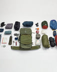Collection of hiking and camping gear arranged around a green backpack on a white background