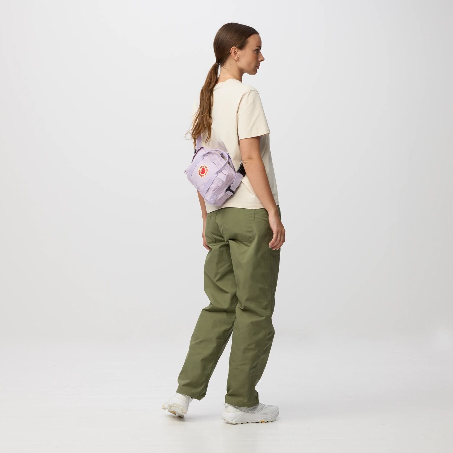 Person wearing green pants and a light-colored shirt with a purple bag on a white background