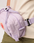 Purple waist bag with a visible brand logo worn by a person on a light background